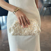 A woman wearing a white dress holds a light gold beaded chain shoulder clutch bag.
