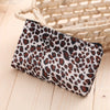A leopard print zippered cosmetic bag resting on a light wooden surface next to a woven basket.