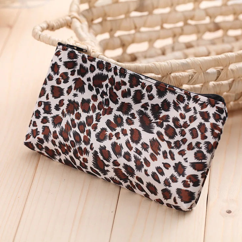 A leopard print zippered cosmetic bag resting on a light wooden surface next to a woven basket.
