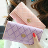 A pink quilted wallet with a gold crown buckle is held by a person.