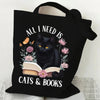 Black canvas tote bag featuring a graphic of a black cat reading a book surrounded by flowers and butterflies.