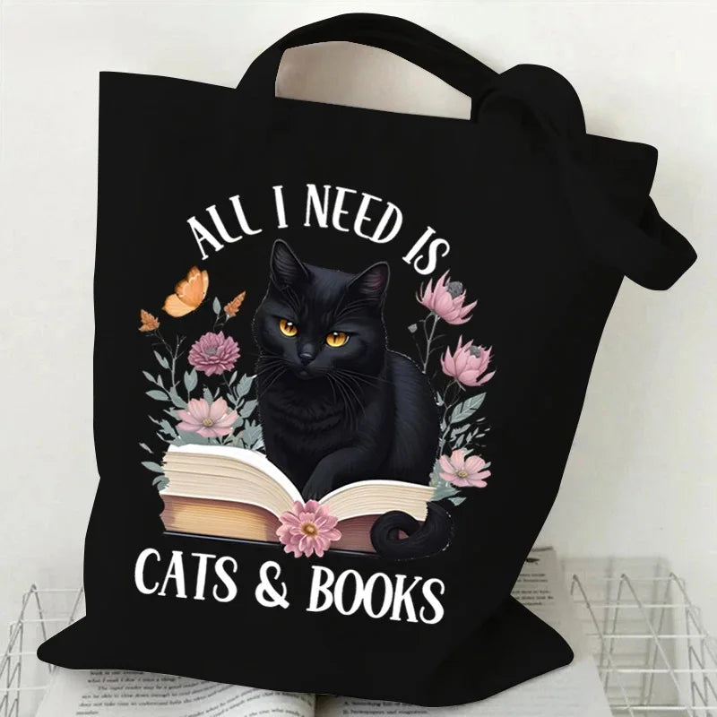 Black canvas tote bag featuring a graphic of a black cat reading a book surrounded by flowers and butterflies.