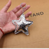 Silver star-shaped leather key chain pendant displayed in a hand against brown paper.