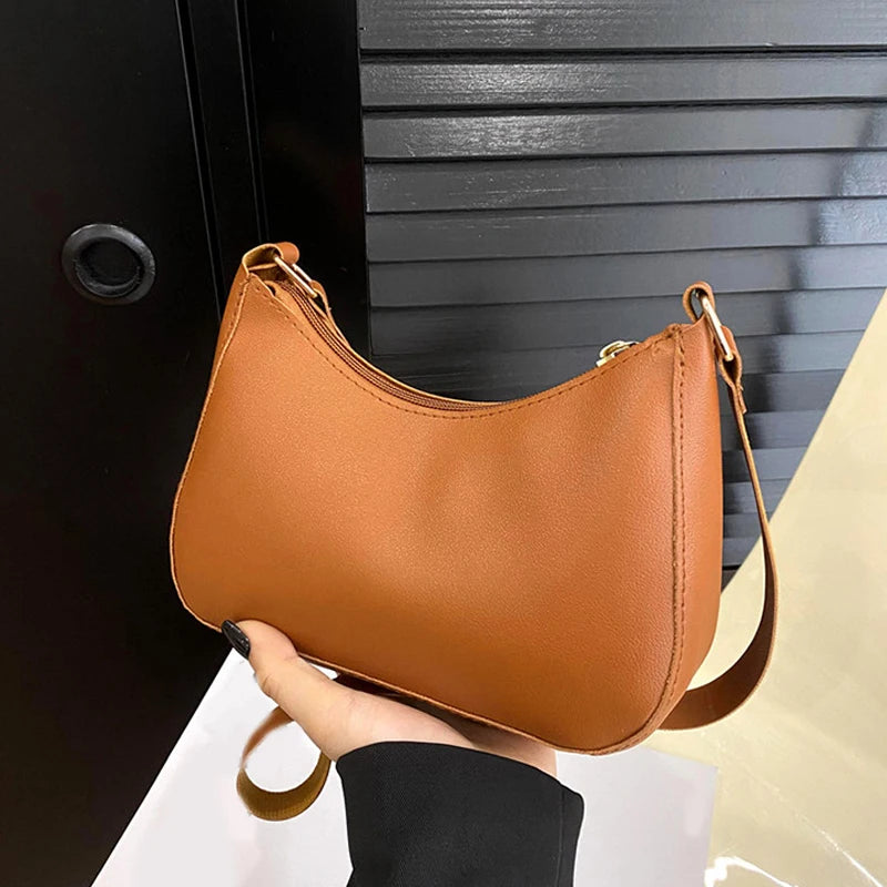 A tan leather shoulder bag with a gold chain strap is held against a black ribbed surface.
