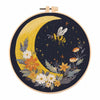 A circular embroidery kit featuring a yellow crescent moon and floral designs on a dark background.