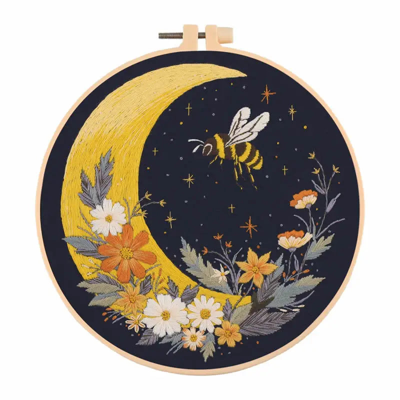 A circular embroidery kit featuring a yellow crescent moon and floral designs on a dark background.