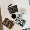 A leopard print cosmetic bag with a black lining and drawstring closure is displayed on a white surface.