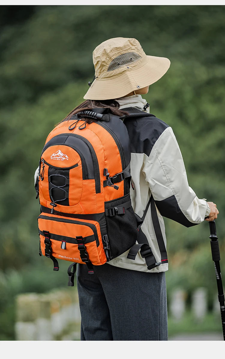 A person wearing a beige hat and a bright orange hiking backpack is shown from the back in an outdoor setting.
