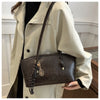 A woman holds a large brown PU leather tote bag against a light beige trench coat.