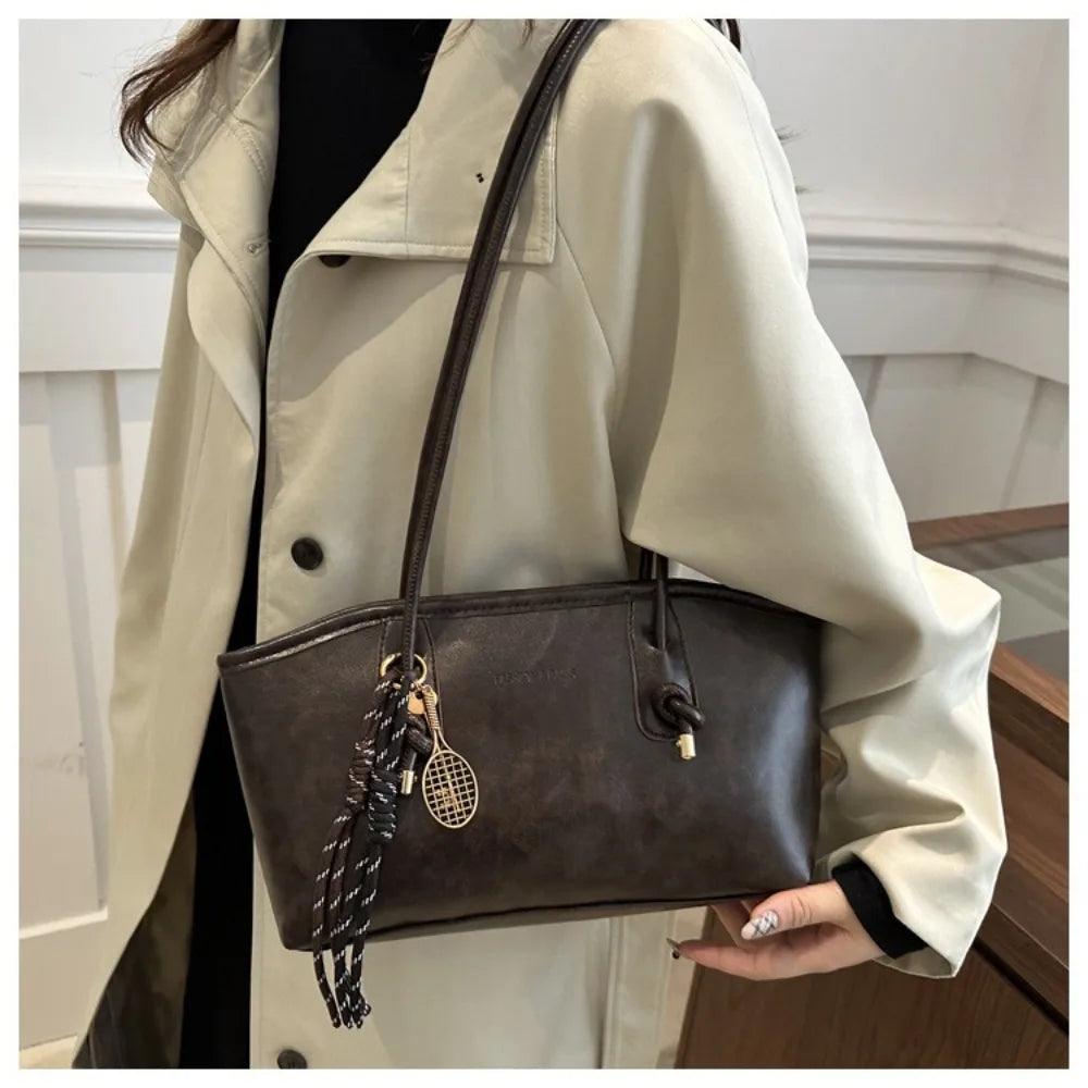A woman holds a large brown PU leather tote bag against a light beige trench coat.