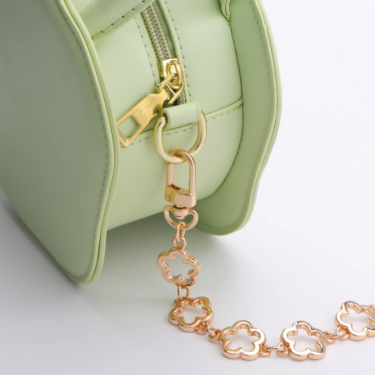 A light green flower bag with a gold-toned extender chain attached to the zipper pull.