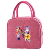 A pink insulated canvas lunch bag featuring a large purple letter M decorated with colorful flowers and foliage.