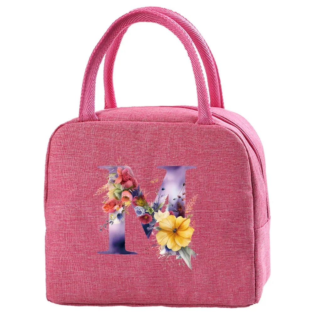 A pink insulated canvas lunch bag featuring a large purple letter M decorated with colorful flowers and foliage.
