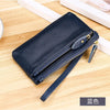 A dark navy blue genuine leather wristlet clutch wallet with a zipper closure resting on a wooden surface.