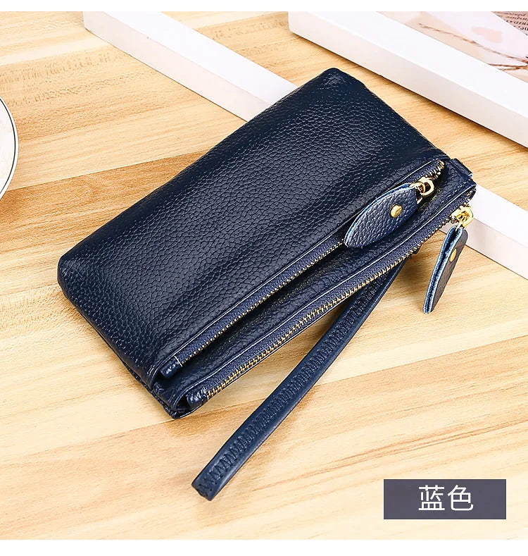 A dark navy blue genuine leather wristlet clutch wallet with a zipper closure resting on a wooden surface.
