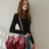 Eine Frau präsentiert eine maroon-Vintage-Leder-Schultertasche mit rosa Träger und dunkler Kleidung.
