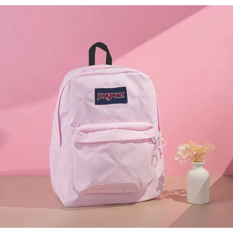 Un sac à dos Jansport rose est exposé contre un mur rose avec une ombre, à côté d'un vase blanc.