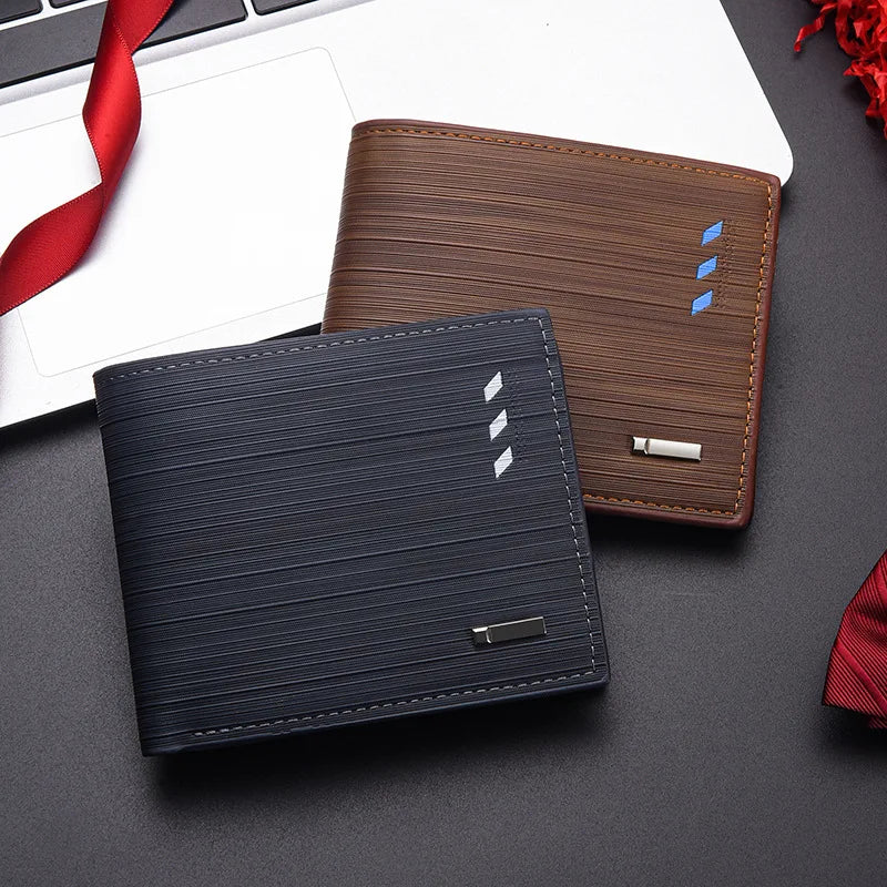 Cartera de cuero azul oscuro y porta tarjetas de cuero marrón, exhibidos sobre una superficie oscura junto a una laptop.