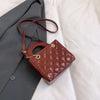 A brown quilted leather crossbody handbag with a gold chain accent resting on a gray blazer.