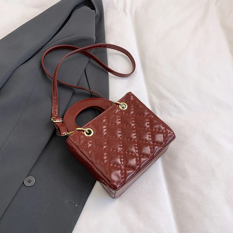A brown quilted leather crossbody handbag with a gold chain accent resting on a gray blazer.