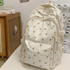Mochila con estampado floral color crema y múltiples bolsillos mostrada sobre una superficie blanca.