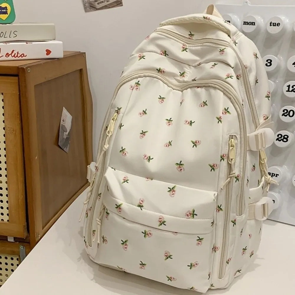 Mochila con estampado floral color crema y múltiples bolsillos mostrada sobre una superficie blanca.