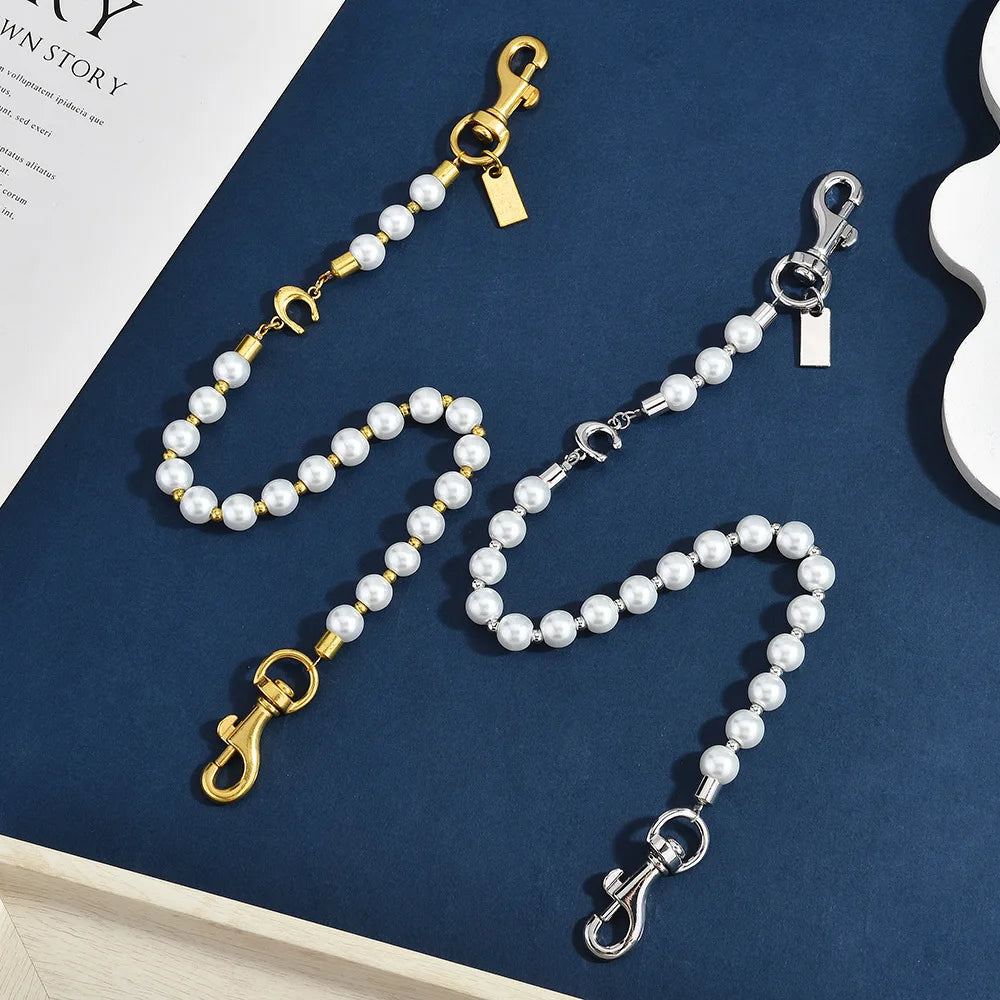 A delicate pearl and gold letter charm necklace with a clasp displayed on a dark blue surface.