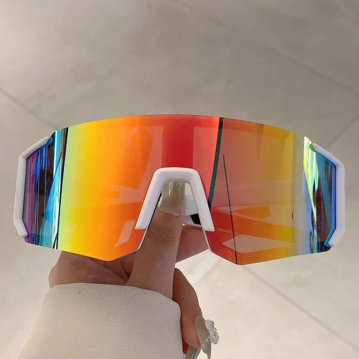 A hand holds a pair of lightweight oversized sunglasses with a gradient lens in various colors.