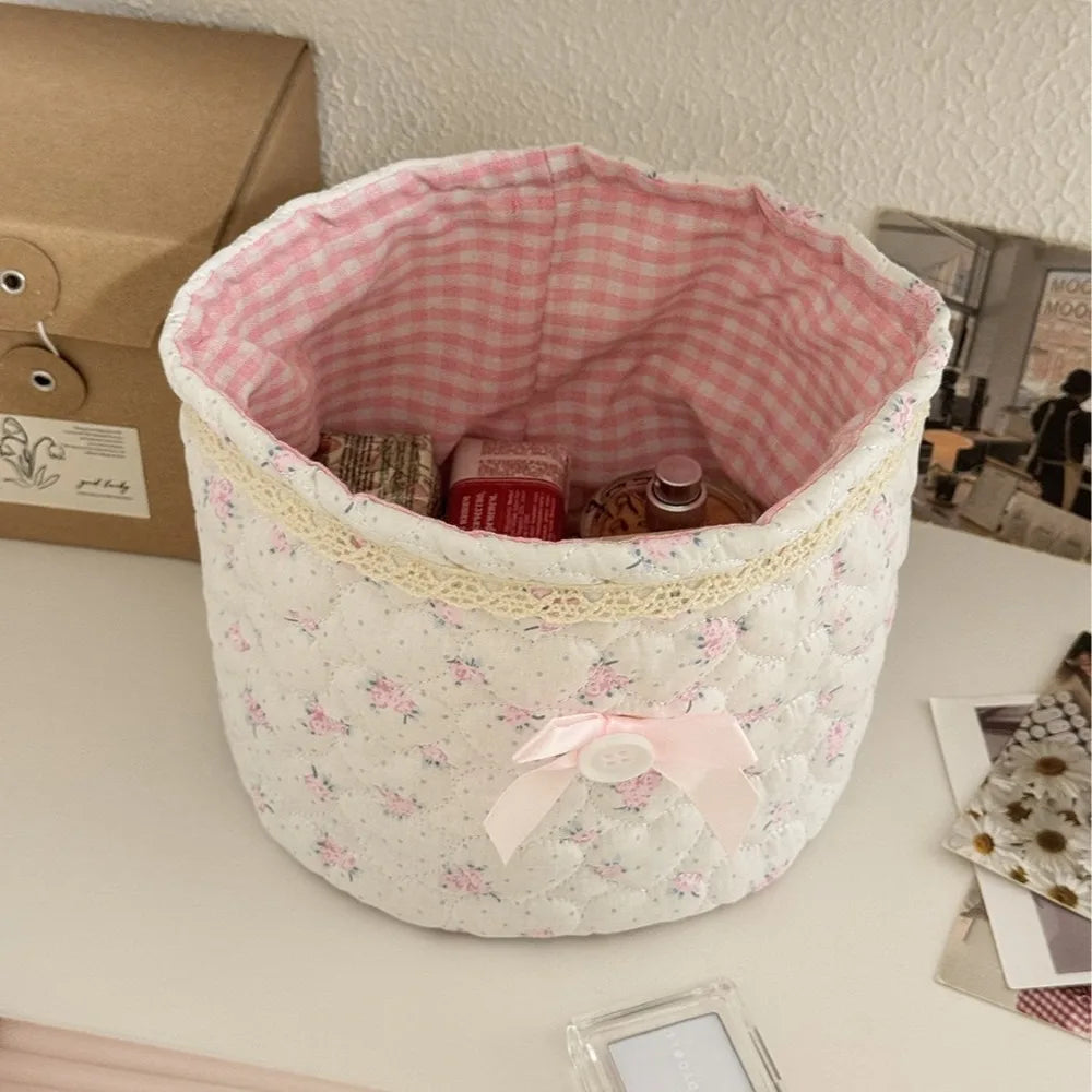 Cesta de almacenamiento acolchada blanca de algodón con forro de cuadros rosa y un lazo de cinta rosa.