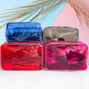 A set of three transparent PVC travel makeup bags in blue, silver, and pink resting on a white surface.