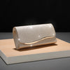 A silver sequined envelope clutch with a gold-toned chain resting on a light wooden surface.