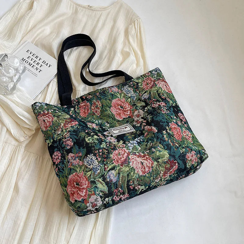 A floral bohemian corduroy tote bag in shades of pink, green, and black resting on a white fabric background.