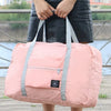 Un sac de voyage pliable rose avec des sangles grises est tenu par une personne à l'extérieur.