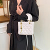 A woman wearing a black dress holds a white diamond grid textured crossbody bag with gold hardware.