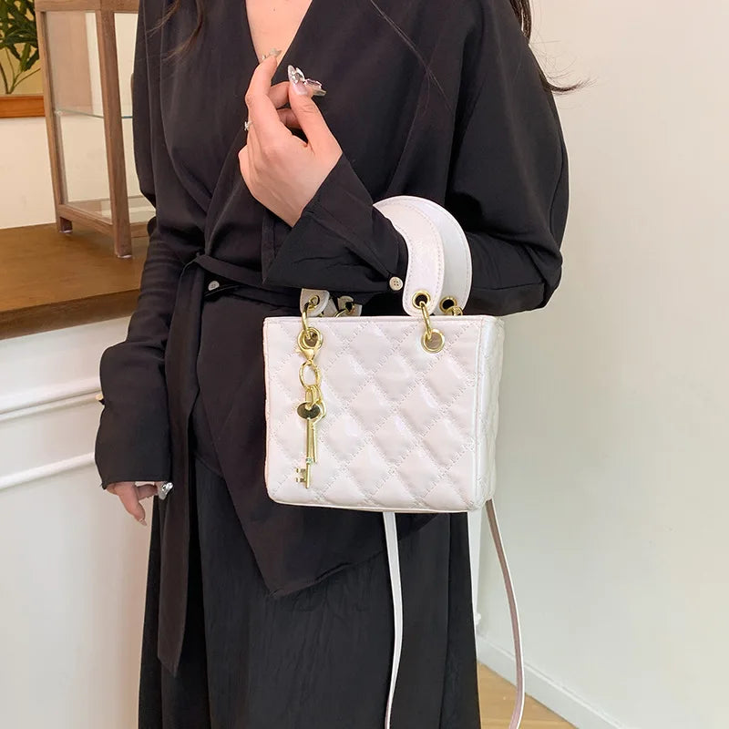A woman wearing a black dress holds a white diamond grid textured crossbody bag with gold hardware.
