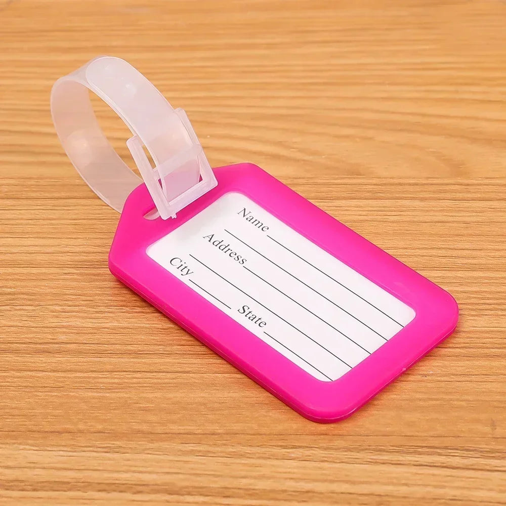 A pink plastic luggage tag with blank lines for name, address, city, and state, attached to a clear strap.