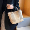 A woman holds a beige canvas crossbody bag with adjustable straps in a dark blazer.