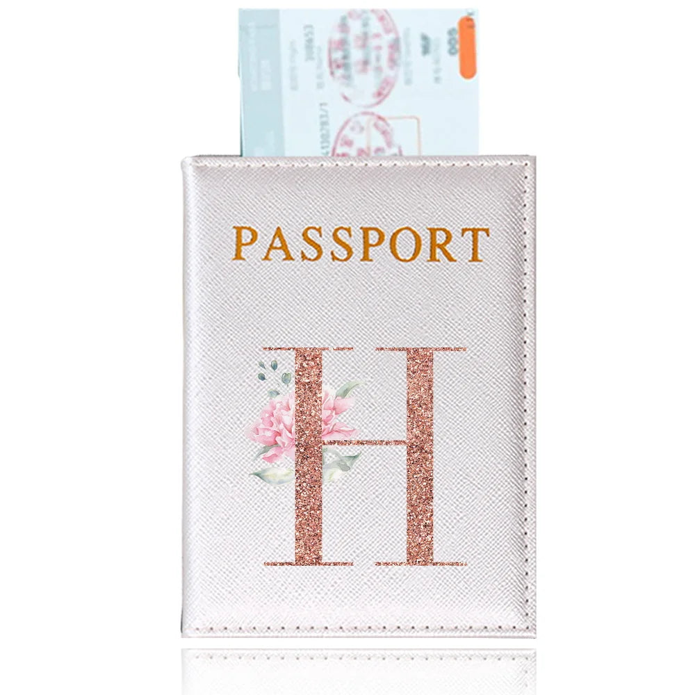 A light pink leather passport holder with gold lettering and a rose-colored initial H