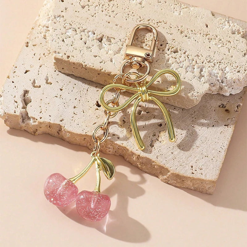 Pendentif clé en forme de cerise rose doré, fixé sur une surface de pierre texturée.