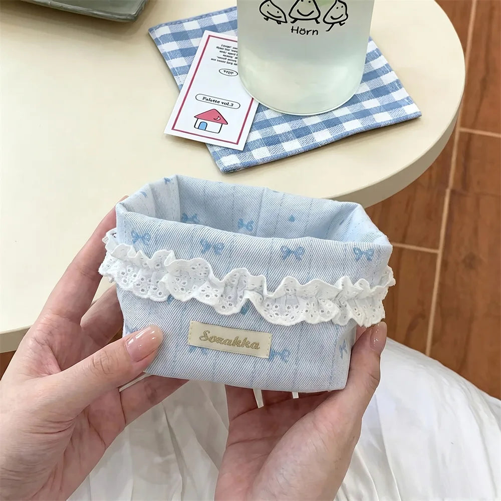 A hand holds a light blue fabric storage basket with white lace trim and a heart pattern.