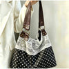 A close-up of a black and white polka dot shoulder bag with a white lace overlay and brown leather straps.