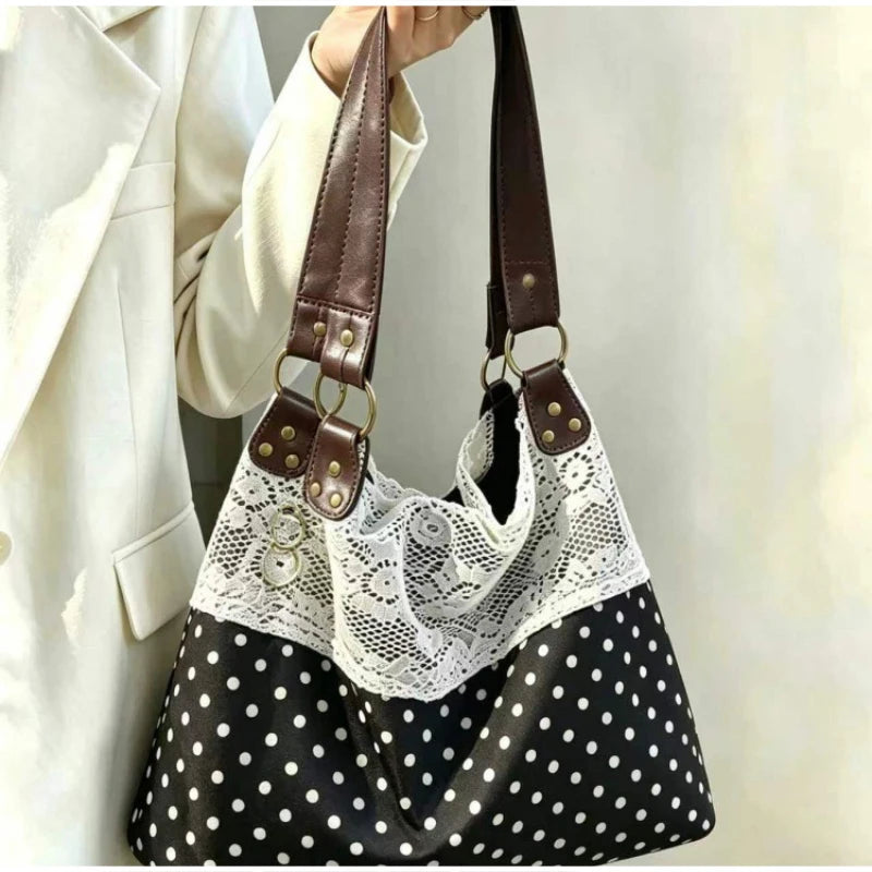 A close-up of a black and white polka dot shoulder bag with a white lace overlay and brown leather straps.