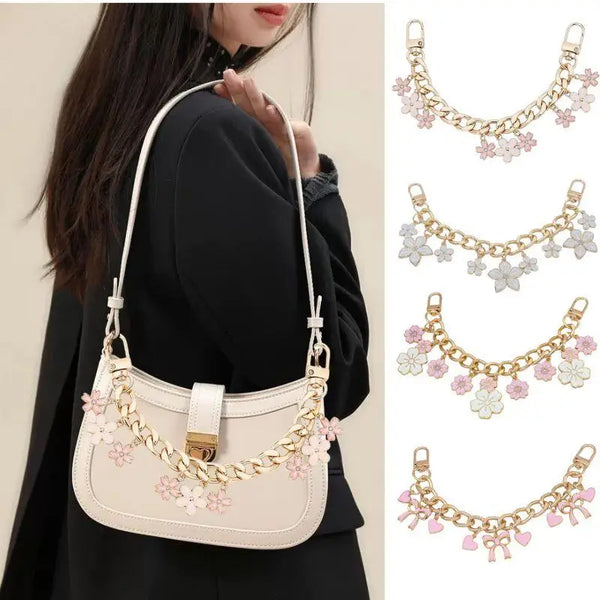 A beige shoulder bag with a gold chain featuring enamel hearts and cherry blossoms.