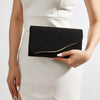 A woman wearing a white dress holds a black velvet evening clutch.
