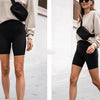 A woman wearing a beige sweater and black athletic shorts holds a black cross-body nylon waist bag.