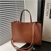 A brown leather tote bag is displayed next to a white slatted blind and a book.