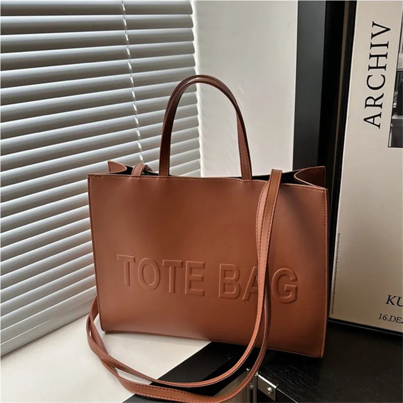 A brown leather tote bag is displayed next to a white slatted blind and a book.