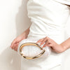 A woman holds an elegant gold-tone evening clutch bag against a white dress.