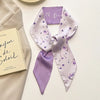 Foulard pour cheveux floral en soie lilas noué en nœud, exposé à côté d'un carnet.