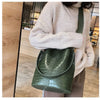 A light beige sweater sleeve holds a dark green alligator pattern leather crossbody bag.